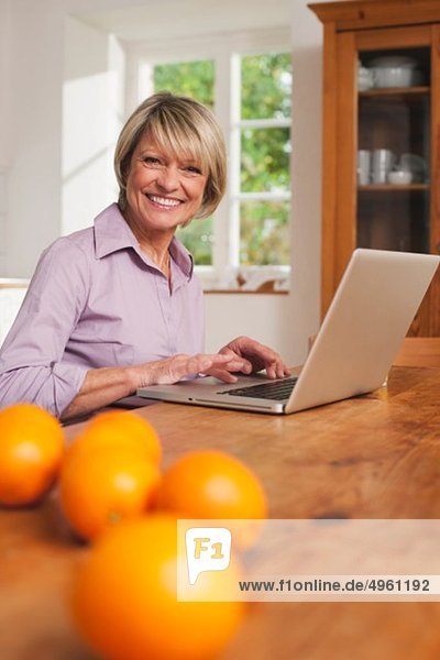 Seniorin mit Laptop und Früchten auf dem Tisch im Vordergrund