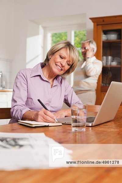 Senior Frau schreibt mit Senior Mann am Telefon im Hintergrund