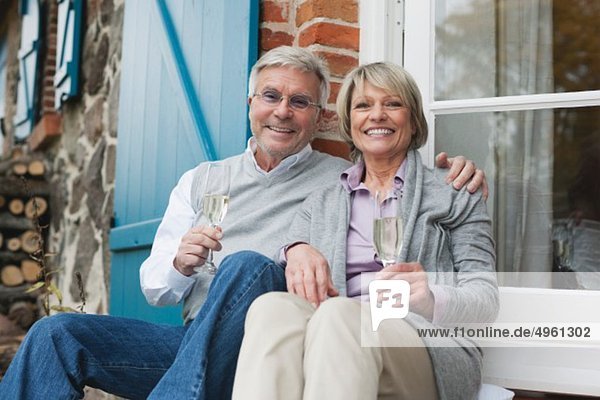 Germany  Kratzeburg  Senior couple sitting on terrace of country house with champagne flute