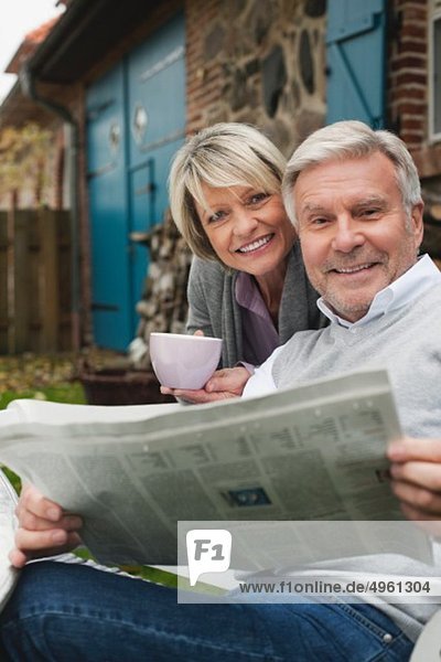 Deutschland  Kratzeburg  Seniorenpaar sitzend auf der Terrasse des Landhauses mit Zeitung