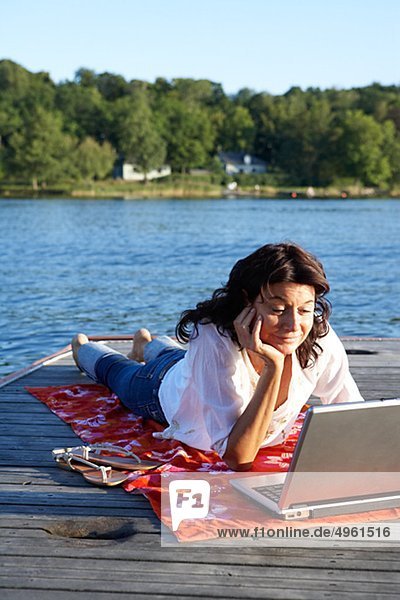 A woman with a laptop on a jetty by a lake  Sweden.