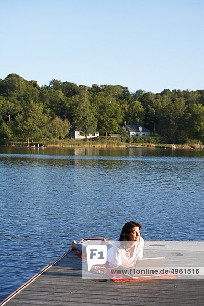 Eine Frau mit einem Laptop auf einer Mole an einem See  Schweden.