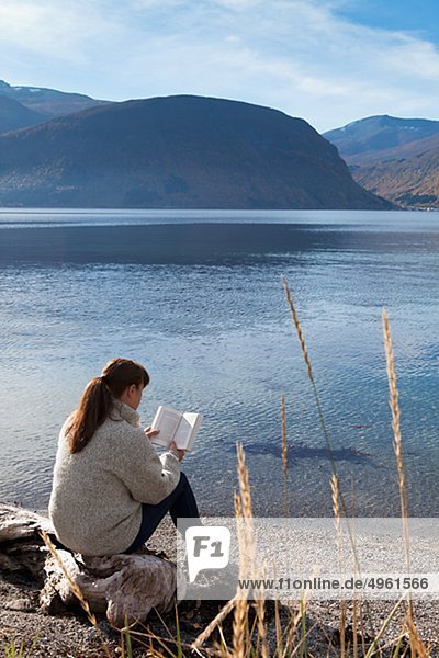 Frau sitzen am Fjord und Buch