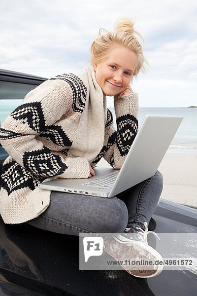 Teenage girl sitting on off road vehicle  using laptop  smiling  portrait