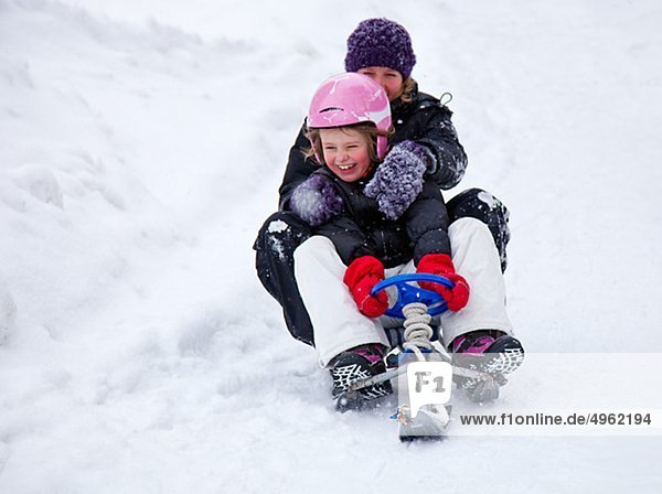 Girl with mother sledging downhill