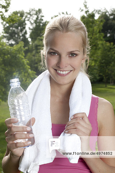 Blonde junge Frau hält eine Flasche Wasser im Freien