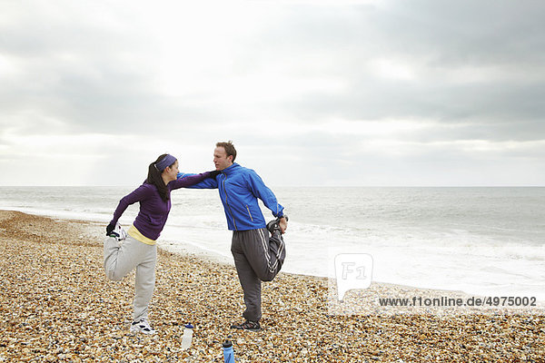 Couple stretching on beach on cloudy day