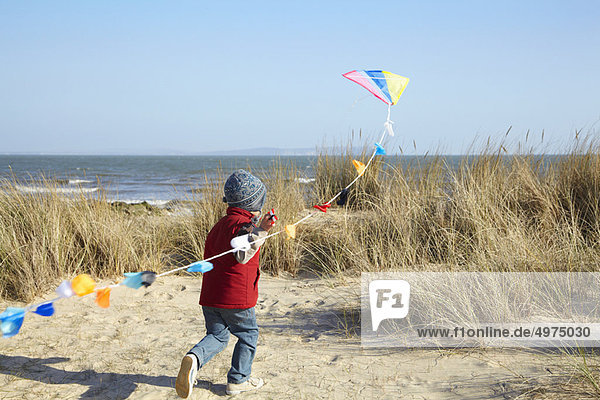Young boy running towards sea with kite