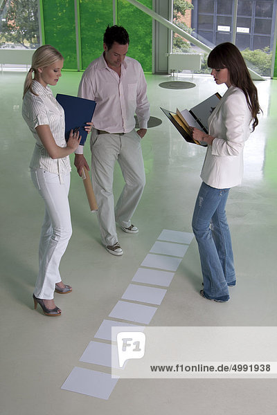 Drei Geschäftsleute schauen auf Unterlagen auf dem Fußboden