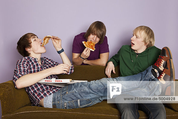 Zwei Teenager  die Pizza essen  während ein anderer neidisch zusieht.