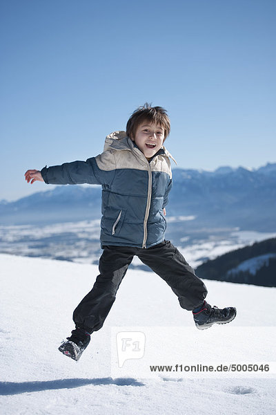 Ein Junge  der auf einen verschneiten Berg springt.