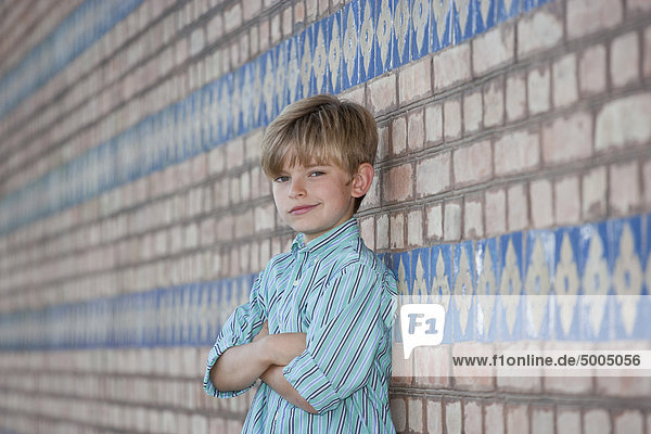 Ein Junge  der sich an eine Wand lehnt und lächelt