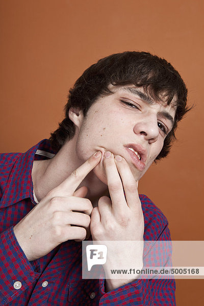 Ein Teenager knallt einen Pickel ins Gesicht  Porträt  Studioaufnahme