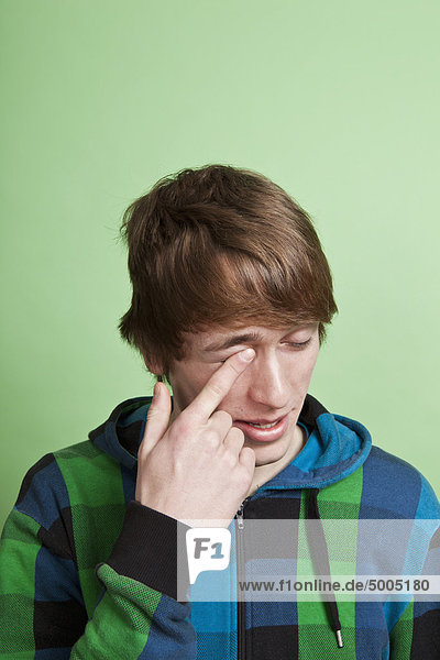 Ein Teenager reibt sich das Auge mit dem Finger,  Porträt,  Studioaufnahme