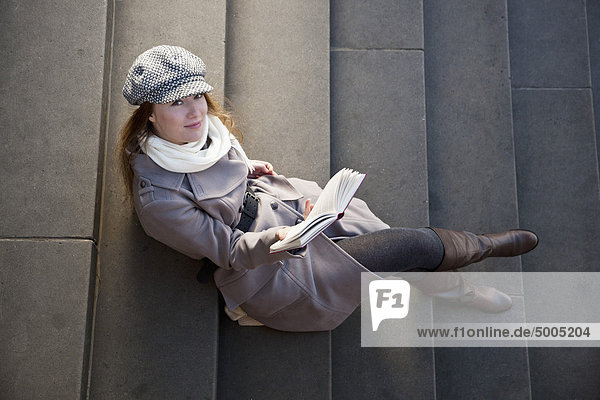 Woman outside on steps with book