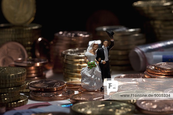 Miniatur-Hochzeitspaarfiguren inmitten von Münzstapeln der Europäischen Union