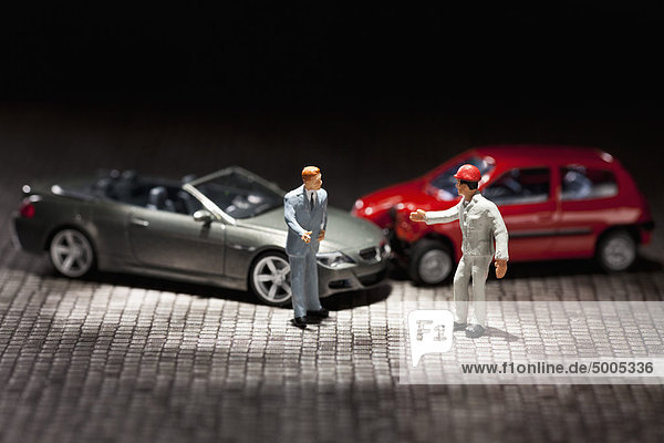 Zwei Miniaturfiguren-Männer streiten sich über ihre Miniatur-Autos.