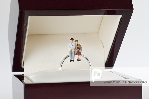 Miniaturfiguren einer älteren Frau und eines älteren Mannes auf einem Ehering sitzend