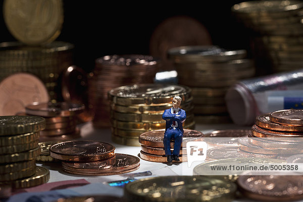 Eine Miniatur-Geschäftsmann-Figur mit gekreuzten Armen auf einem Münzstapel.