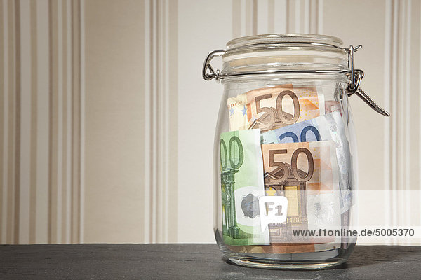 Glasgelddose mit Euro-Banknoten auf einem Tisch