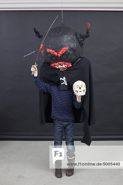 Kind mit Halloween-Outfit  einem Totenkopf in der Hand und einem Spielzeugschwert.
