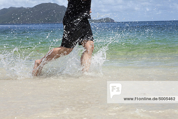 Low section of a man running through the water at a beach