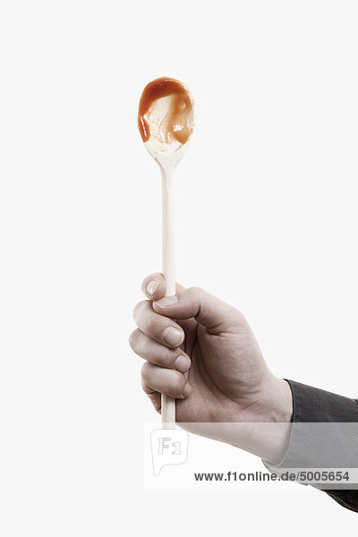 A man holding aloft a wooden spoon with red sauce on it