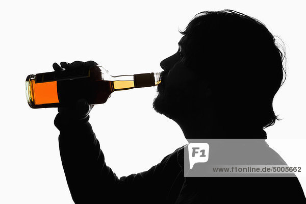 Ein Mann mit Silhouette  der Whiskey aus der Flasche trinkt.