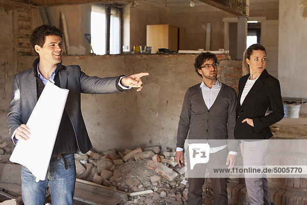 Ein Architekt zeigt ein Paar auf einer Baustelle