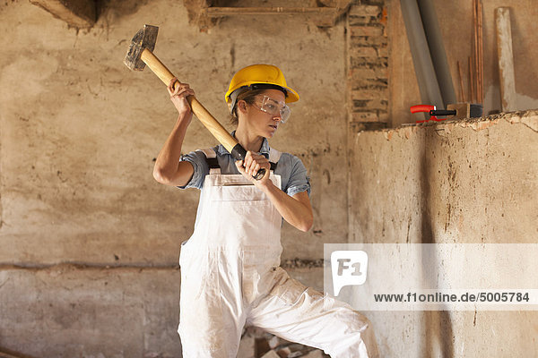 Eine Bauarbeiterin  die einen Vorschlaghammer schwingt.
