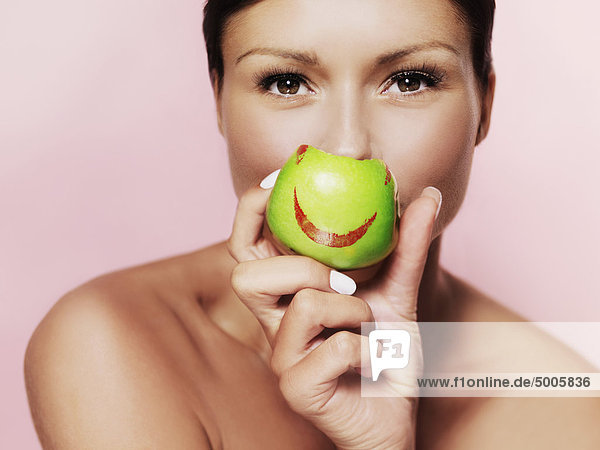 Eine Frau  die einen grünen Apfel mit einem leuchtend roten Lippenstift drauf hält.