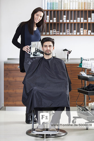 Ein Friseur hält einen Spiegel für den Kunden hoch.