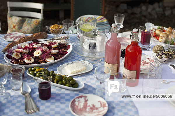 Esstisch im Freien mit Geschirr und Lebensmitteln wie Oliven und Ziegenkäse