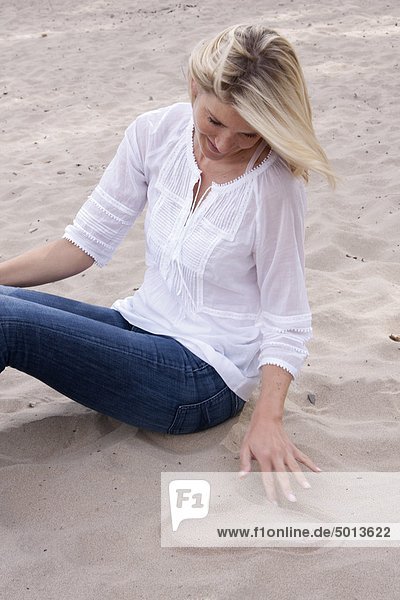 Blonde Frau zeichnet ein Herz in den Sand