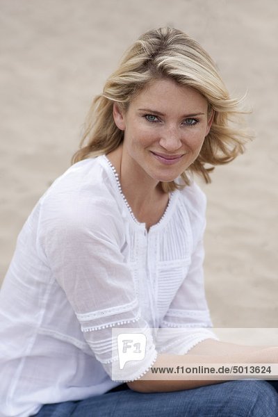 Blonde Frau sitzt im Sand