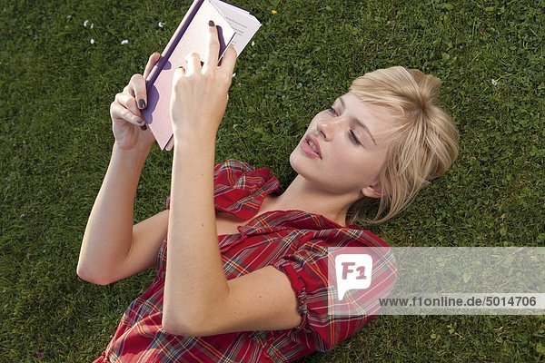 Junge blonde Frau liest ein Buch im Gras