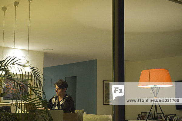 Mann mit Laptop im Wohnzimmer, durchs Fenster gesehen