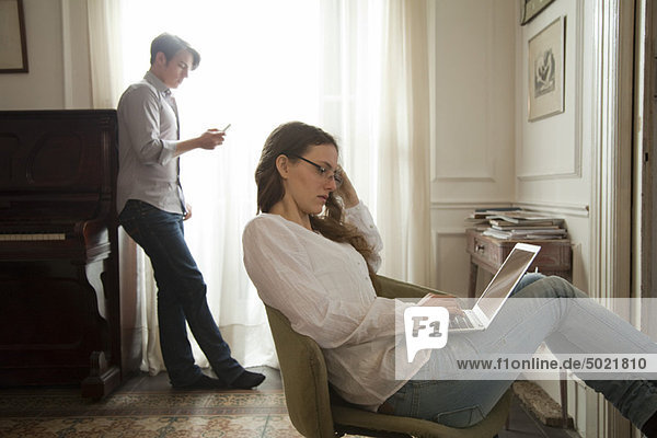 Woman using laptop computer at home  man holding cell phone in background