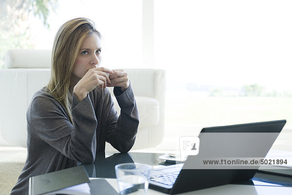 Woman sitting at coffee table with laptop computer  drinking coffee