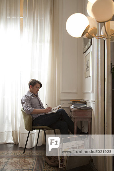 Mann sitzt am Schreibtisch und liest Magazin