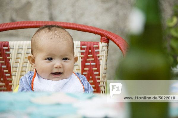 Baby sitzend auf einem Stuhl lächelnd
