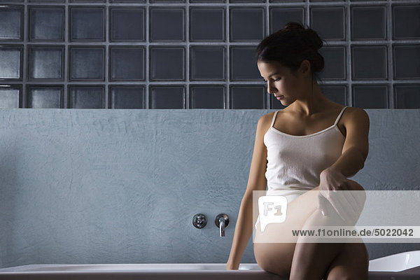 Frau sitzt auf Badewannenrand in Unterwäsche