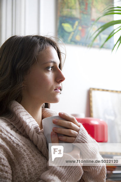 Junge Frau hält Kaffeetasse  schaut in Gedanken weg