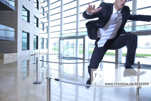 Businessman jumping over ropes in lobby