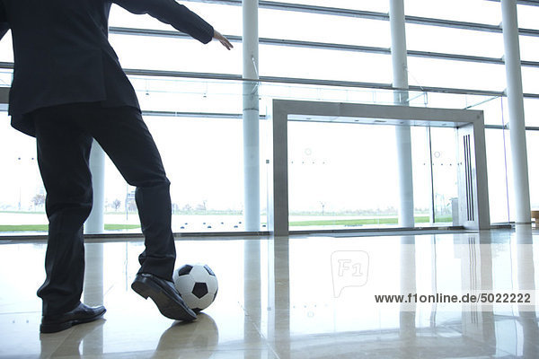 Businessman kicking soccer ball in lobby