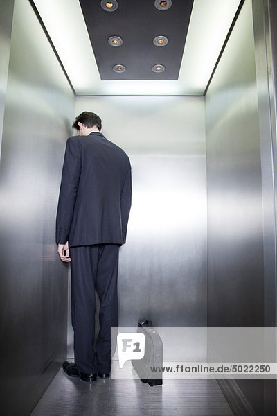 Geschäftsmann steht in der Ecke des Aufzugs mit Rücken zur Kamera und Kopf nach unten