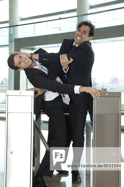 Businessmen fighting to beat each other through turnstile