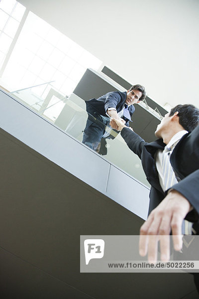 Businessman leaning over balcony  holding on to colleague's hand