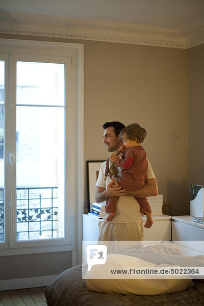 Father holding toddler son  looking out window