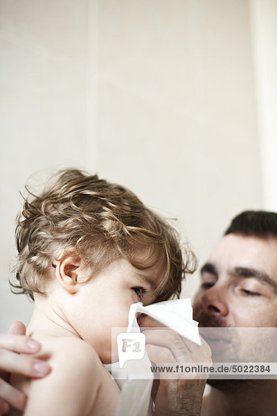 Vater hilft Kleinkind Sohn putzen seine Nase